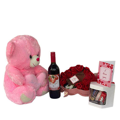 Pink teddy bear, bottle of wine, heart-shaped box of chocolates, and small gift bag on a white background