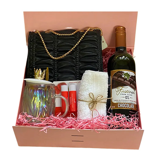 Gift basket with black handbag, wine bottle, mug, and other items in a box.
