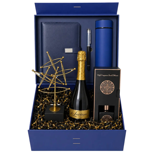 A luxury gift set in a navy blue box, featuring a bottle of Lucum champagne, a gold geometric sculpture, a black and gold diffuser box, a blue cylindrical container, and a pen, all arranged on a white background.