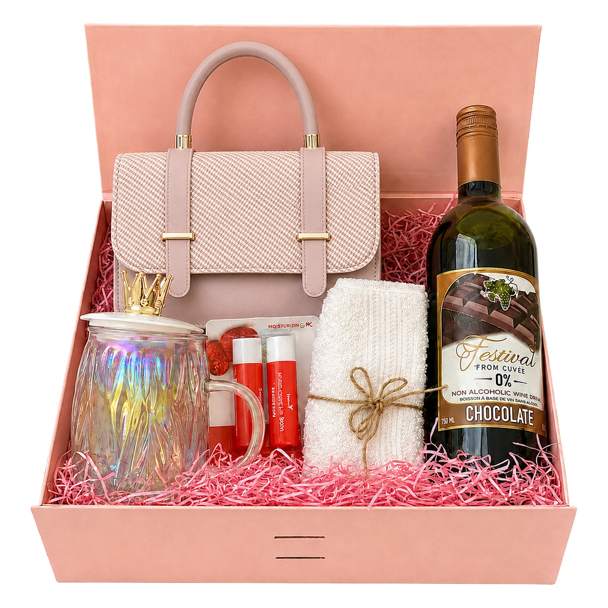 A curated gift box set containing a light pink textured handbag, a bottle of chocolate-flavored non-alcoholic wine, a white knit scarf tied with twine, a glass mug with an iridescent lid, and two red lip balm tubes, all arranged in pink shredded paper inside a pink box.