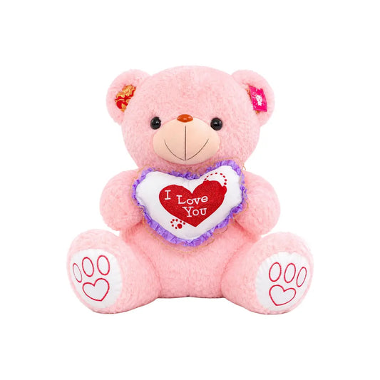A pink plush teddy bear sitting and holding a white heart-shaped pillow with red trim and the words 'I Love You' in red. The bear has embroidered red paw prints on its feet and small decorative flowers in its ears, shown against a plain white background.