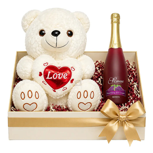 A Valentine's Day gift box set featuring a white plush teddy bear holding a red heart with 'Love' written on it, next to a bottle of Pinac Grapefruit Sparkling Red Wine, all arranged in a cream-colored box with a gold ribbon and red decorative filler.