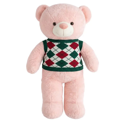 A pink plush teddy bear wearing a green, red, and white argyle sweater vest, set against a plain white background.