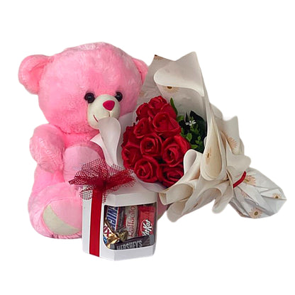 Pink teddy bear, red roses, and white high heels with a box of chocolates on a white background