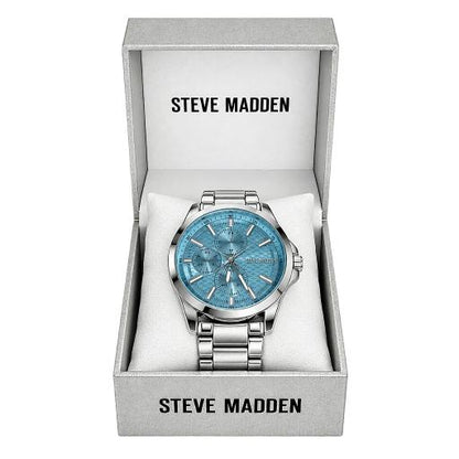 Steve Madden men's analog watch with a silver stainless steel case and bracelet, featuring a textured light blue dial, presented inside its open light gray gift box.